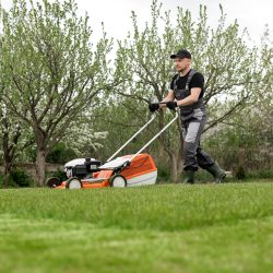 Landscaping supervisor providing hands-on staff training to a crew member on proper equipment use and worksite safety practices