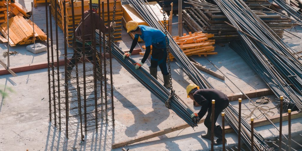 Construction Crew at Work, Dedicated workers skillfully handle steel rods and materials on bustling construction site, teamwork and essence of structural development
