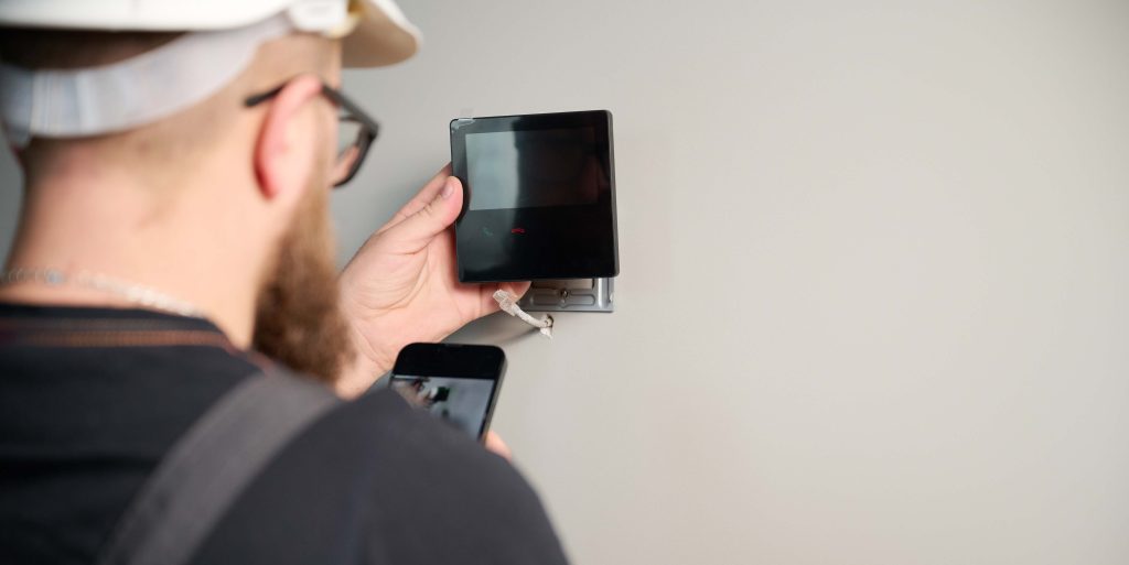 Security alarm installation. Security technician installing safe monitor on wall in the new office. Installing security system. Man worker installing alarm technology insurance in home