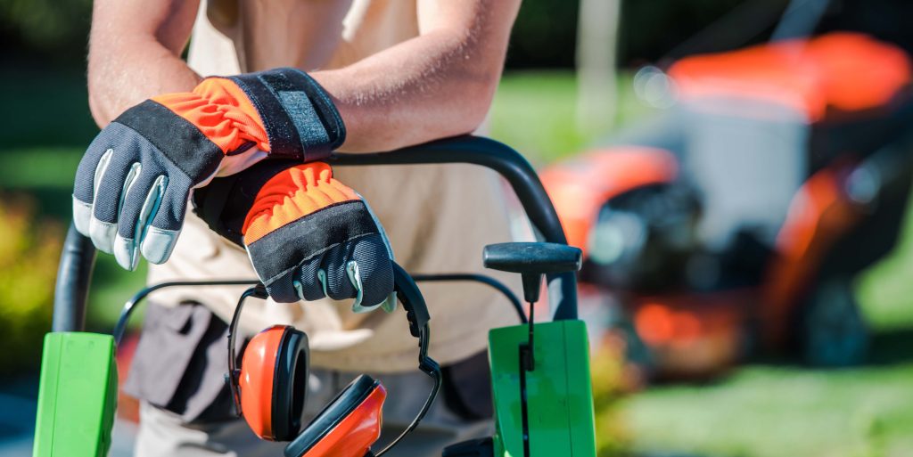 Landscaping Contractor Work Landscaping worker in a high-visibility safety vest and gloves operating lawn maintenance equipment on a commercial property