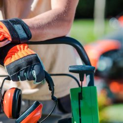 Landscaping worker in a high-visibility safety vest and gloves operating lawn maintenance equipment on a commercial property