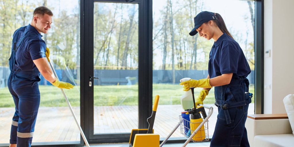 During cleaning house with big panoramic window Janitorial worker mopping a commercial hallway floor with a professional mop and bucket with wet floor safety signs visible