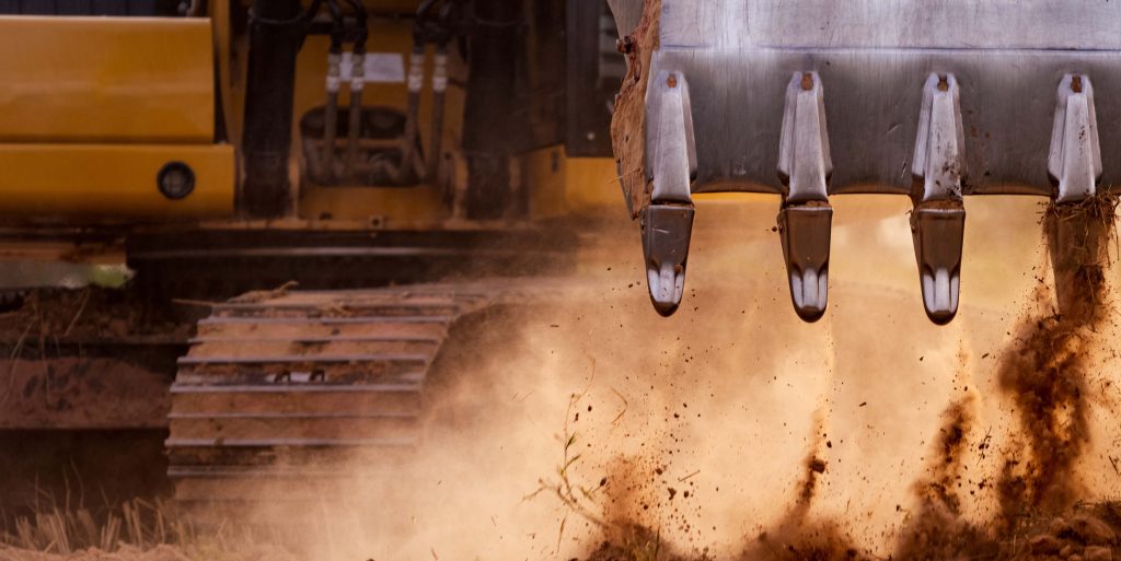 Selective focus on metal bucket teeth of backhoe digging soil. B