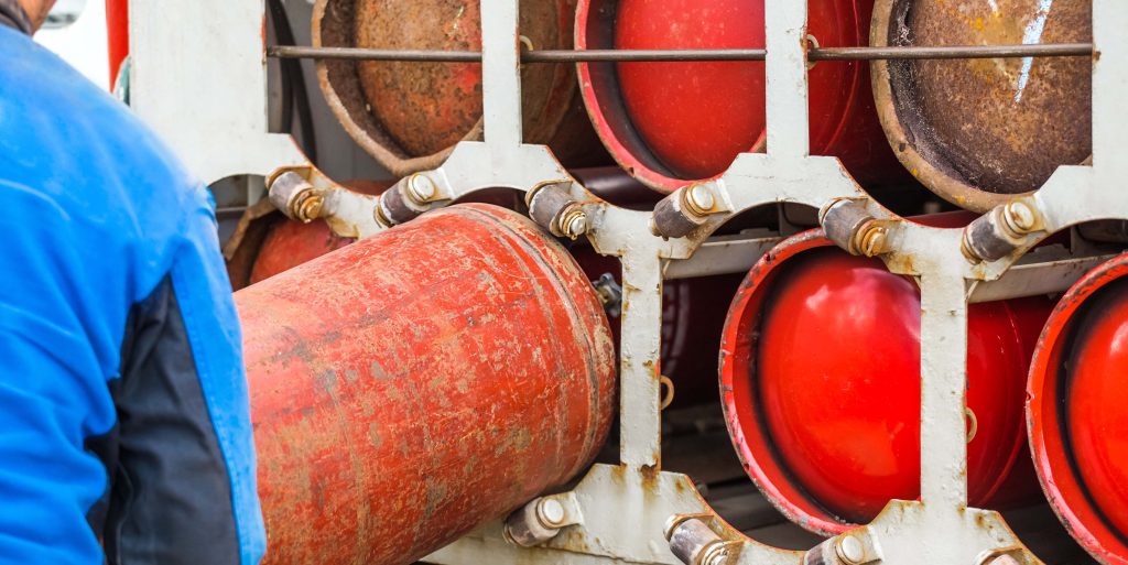 Male industrial worker puts a gas cylinder into a gas machine. Equipment for the safe transportation of propane gas bottles