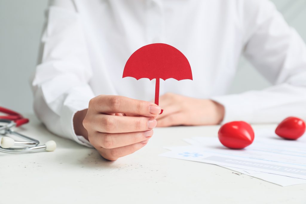 Woman with umbrella figure and health insurance form at table, closeup someone in a white shirt holding a small red umbrella