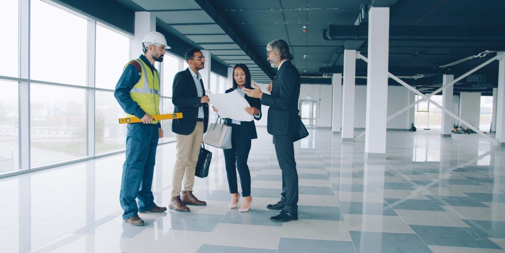 Multi-ethnic group of businesspeople talking and studying blueprint indoors in modern commercial building Tree care worker in full PPE including hard hat, safety harness, and chainsaw gear working safely high up in a large tree