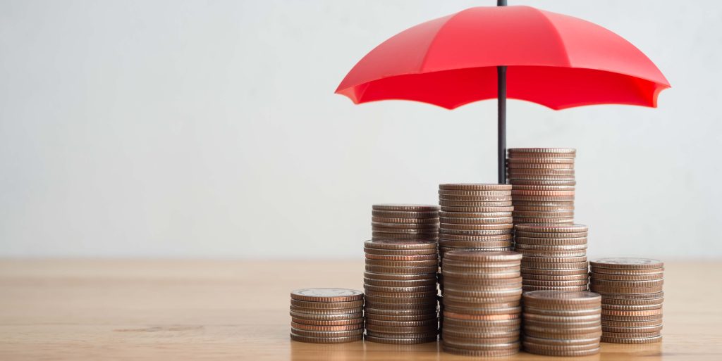 Stacked coins is protected by red umbrella on wooden table white
