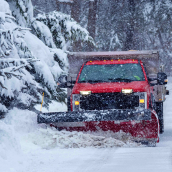 Red snow plow truck clearing a snow-covered road during a winter storm, highlighting snow removal operations and liability risks for landscaping contractors.