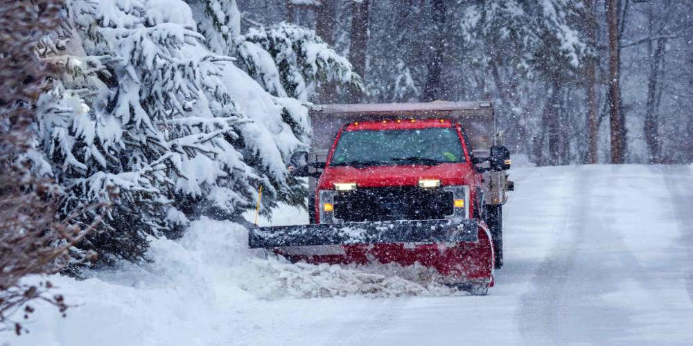 Blog-Image-Crop-1000x500 - September 05, 2025 at 10.16.33 (1) (7) Red snow plow truck clearing a snow-covered road during a winter storm, highlighting snow removal operations and liability risks for landscaping contractors.