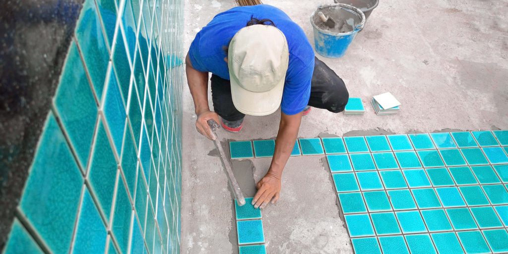 Tiled pool. The man hand while using spacer for installing tiles
