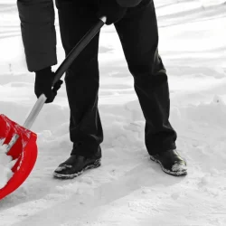 A worker clearing snow with a red shovel under a snow removal contract