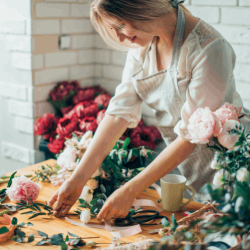 Florist arranging a colorful fresh flower bouquet at a flower shop counter surrounded by blooms and greenery displays