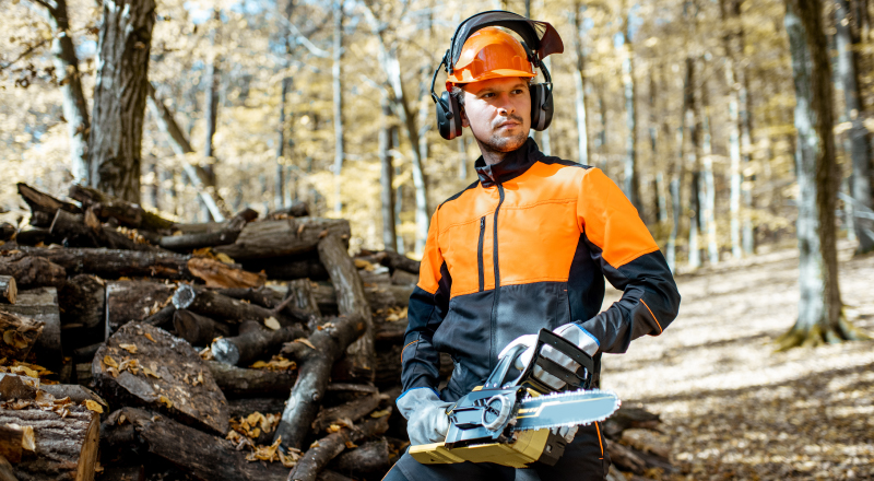 arborist-with-chainsaw Arborist standing with chainsaw near log pile