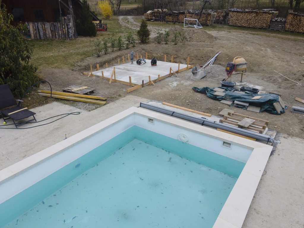 Drone shot of pool construction site with concrete pad for heat pump and pool house in garden