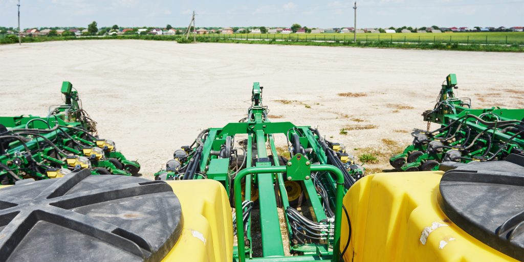 Close-up of a hydroseeding or broadcast seeder attachment mounted on a tractor spreading seed across an open agricultural field
