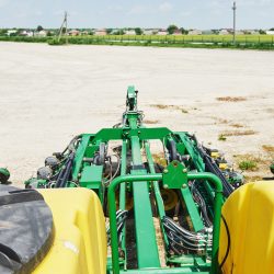 Close-up of a hydroseeding or broadcast seeder attachment mounted on a tractor spreading seed across an open agricultural field