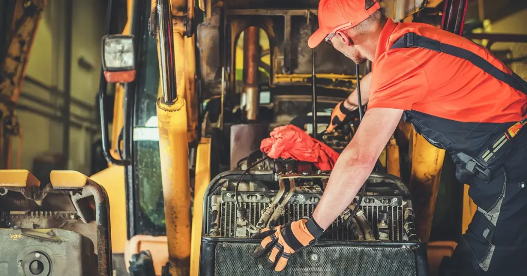 Mechanic performing heavy equipment maintenance on a yellow excavator engine. Mechanic performing heavy equipment maintenance on a yellow excavator engine.