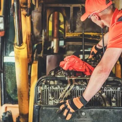 Mechanic performing heavy equipment maintenance on a yellow excavator engine.