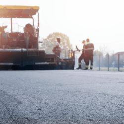 Road construction crew with equipment and warning cones actively managing a paving project along a public roadway