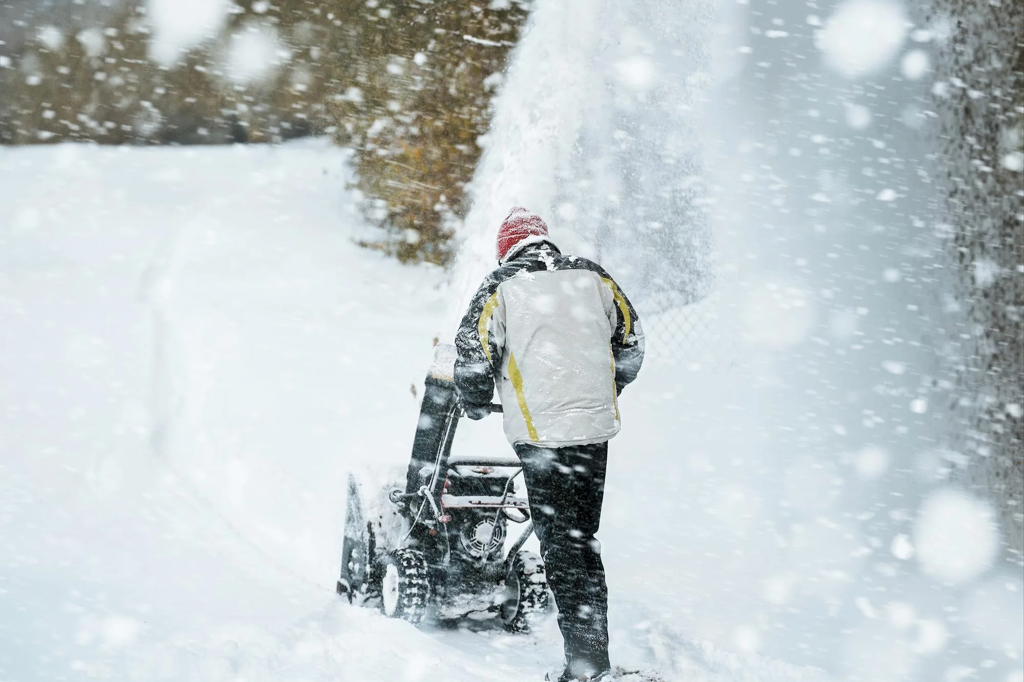 A crew member using a snow blower to clear a lot after a winter storm