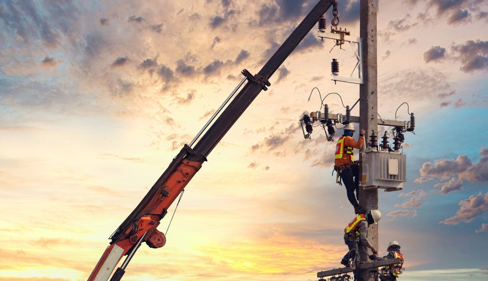Utility workers repairing power lines using specialized equipment at sunrise, emphasizing teamwork and the critical nature of infrastructure maintenance.