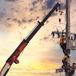 Utility workers repairing power lines using specialized equipment at sunrise, emphasizing teamwork and the critical nature of infrastructure maintenance.
